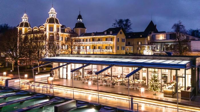 Illuminated building with a restaurant terrace and a large illuminated building in the background at night.