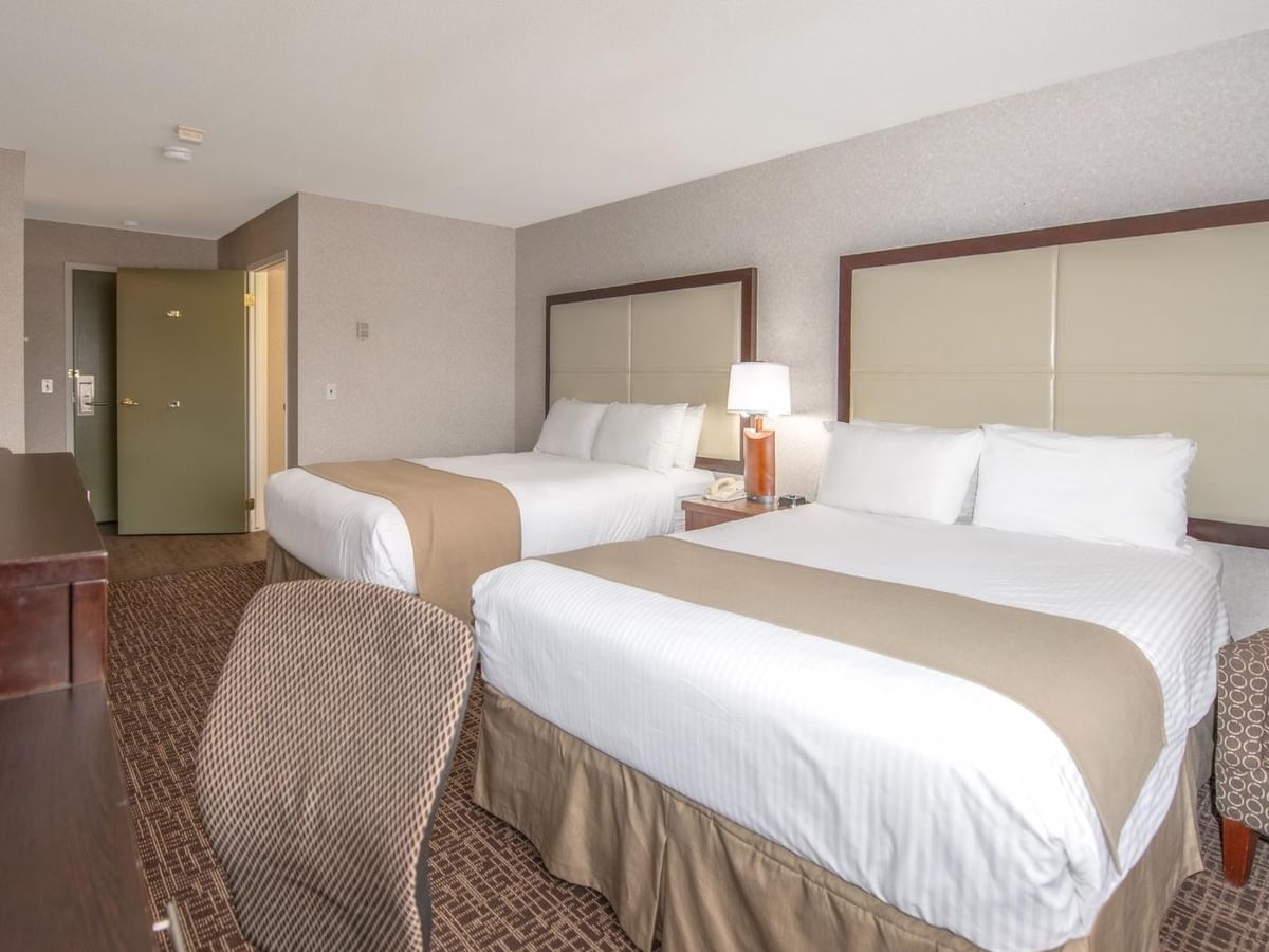Hotel room with two beds, nightstand with lamp, TV, and two chairs.