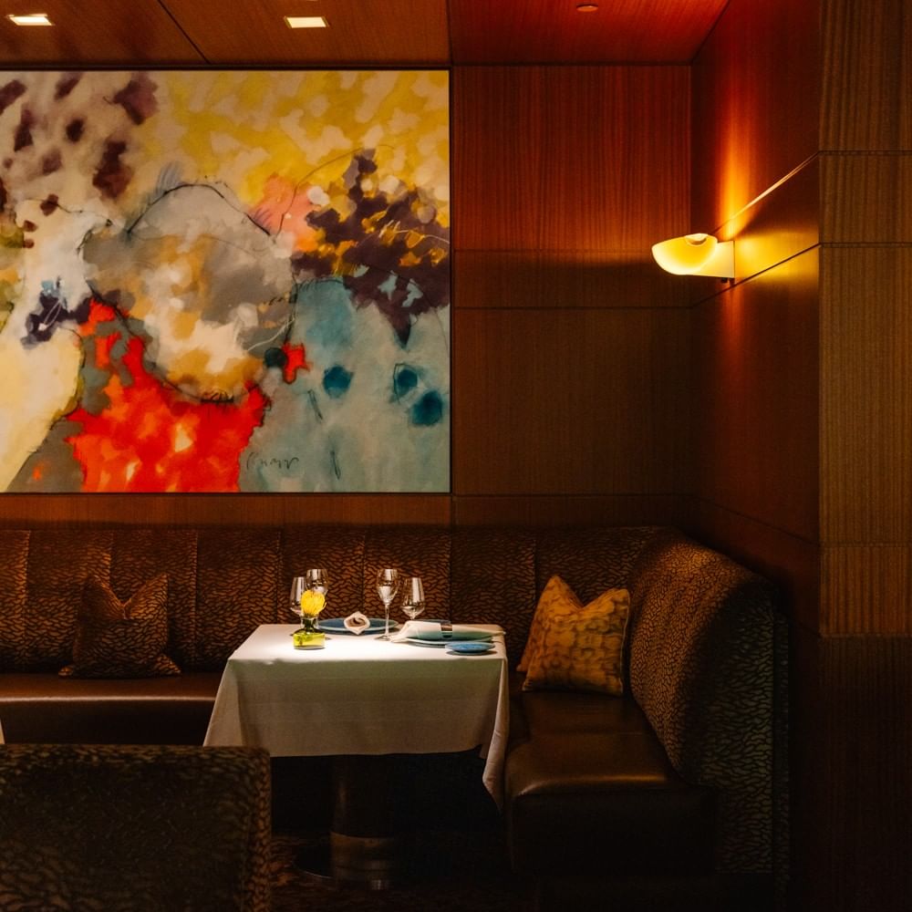 Intimate dining booth with abstract artwork, warm lighting, and table set with wine glasses for Herons x Enclos event.