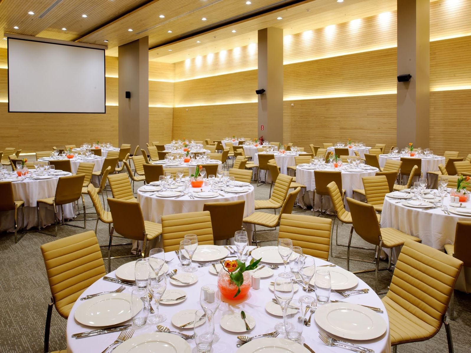 Round tables with white tablecloths, plates, and cutlery set up at the Mayo Ballroom at the NOI Hotel Vitacura.