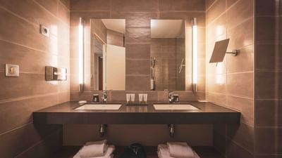 A bathroom with two sinks, large mirror, tiled walls, and two sets of folded towels.