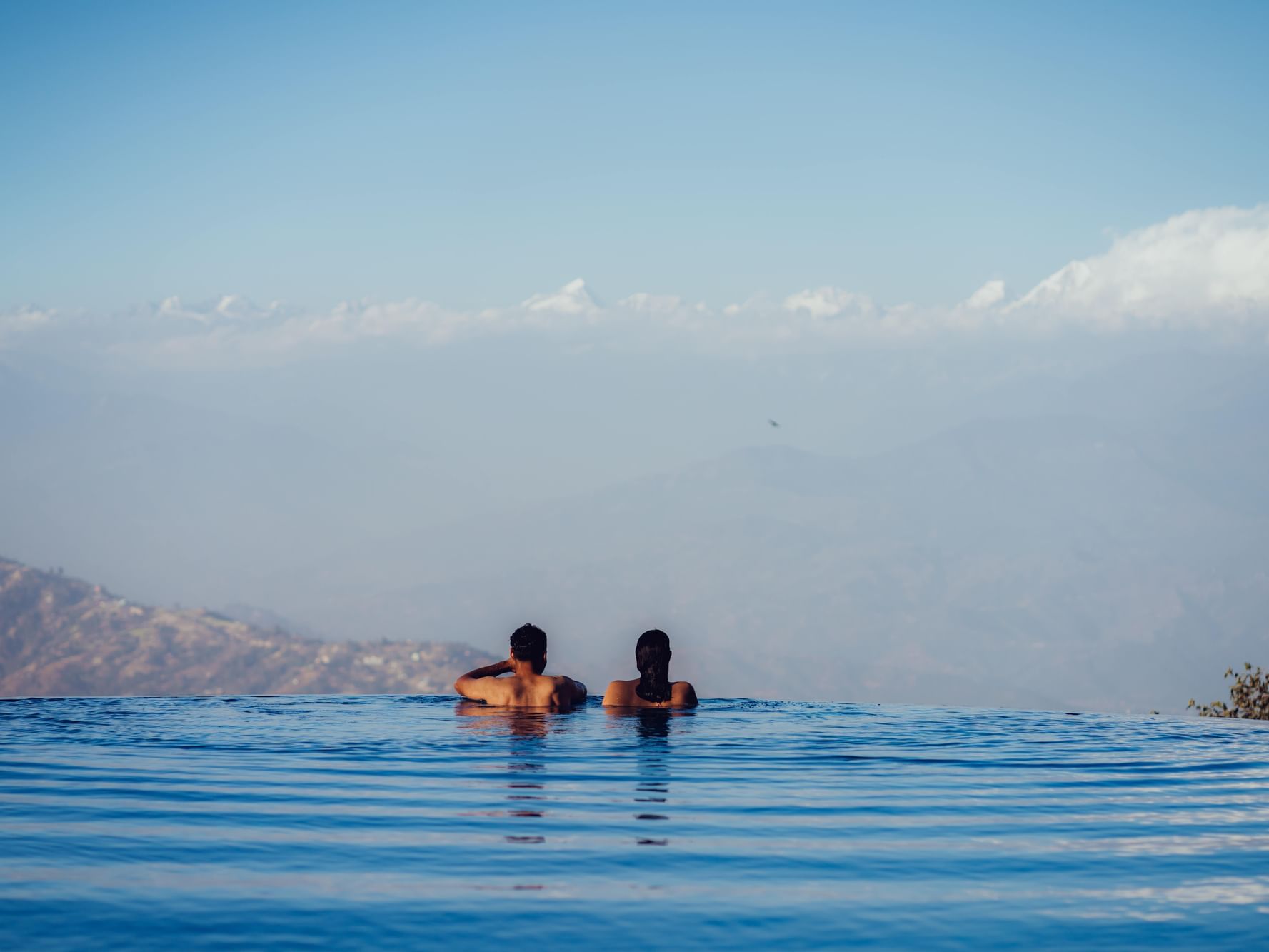 Couple relaxing in an infinity pool, overlooking misty mountains and a clear sky at Dwarika's Himalayan Wellbeing