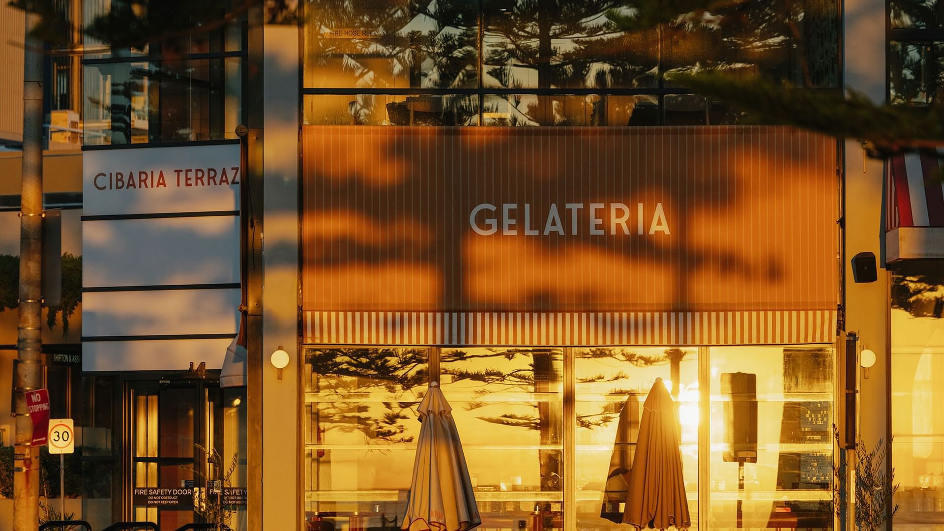 Cibaria Caffetteria & Gelateria at Elysium Manly storefront with umbrellas by a window under a striped awning