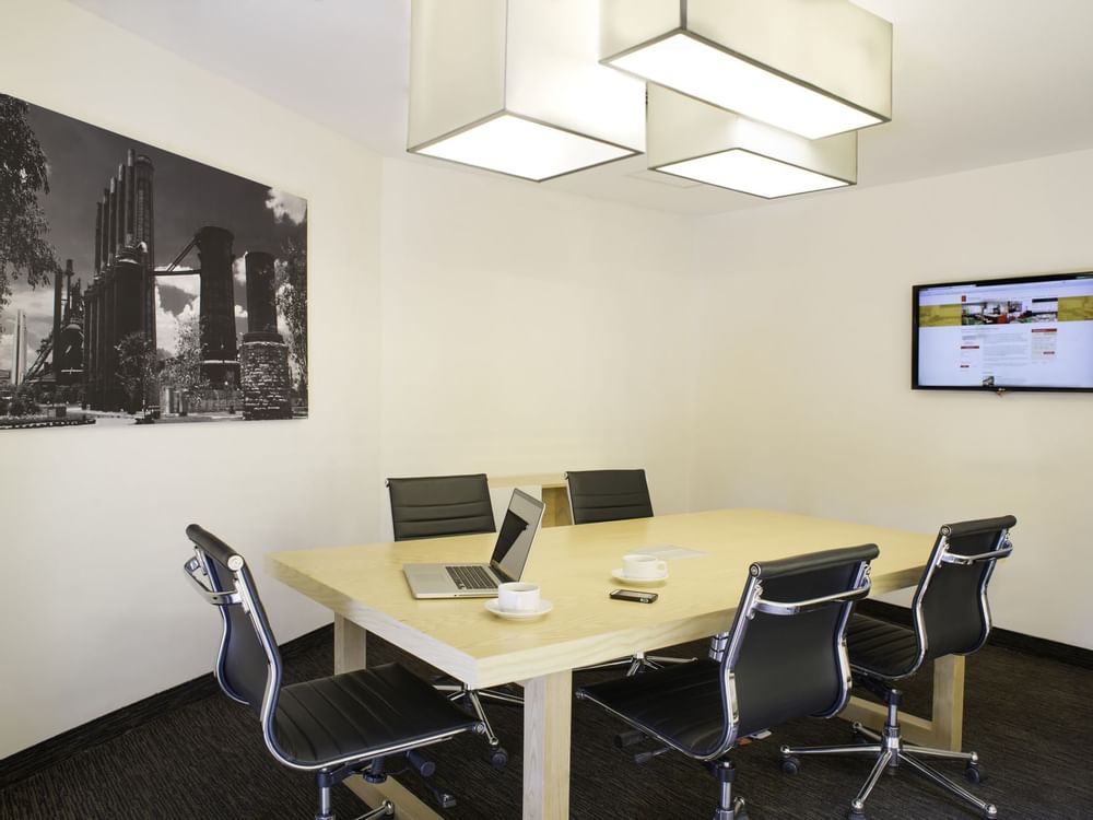 Modern Fiesta Inn business center with wooden table, 6 black leather chairs, laptop, coffee cups, smartphone