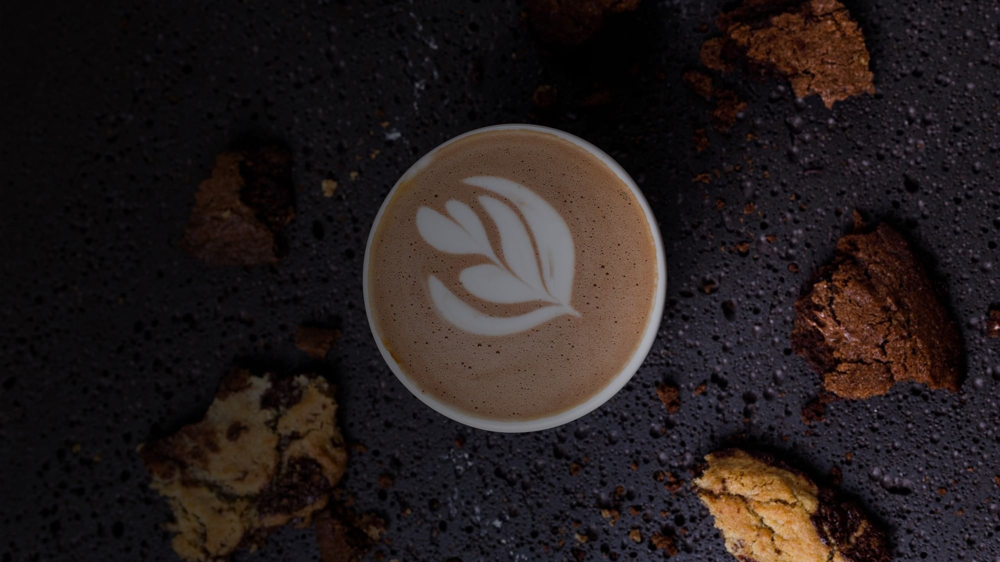 A cup of coffee with latte art surrounded by cookies at Camino Real Guadalajara