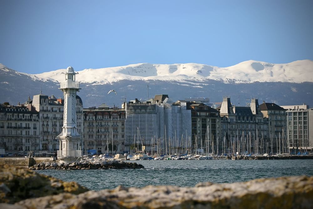 Les Pâquis Lighthouse by a harbor under snow-capped mountains near Warwick Geneva