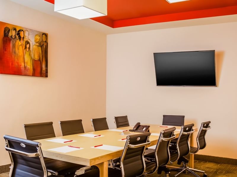 Modern Fiesta Inn meeting room with wooden table, 6 black leather chairs, laptop, coffee cups, smartphone