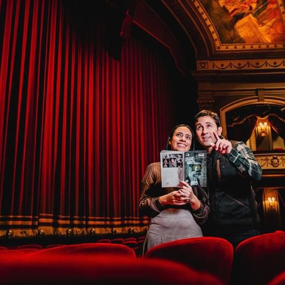 Couple holding a playbill booklet inside a grand theater auditorium room near Spencer Hotel & Conference Centre