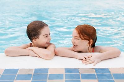 Two smiling girls leaning on edge of pool at Rodd Royalty, premier among charlottetown hotels with pools