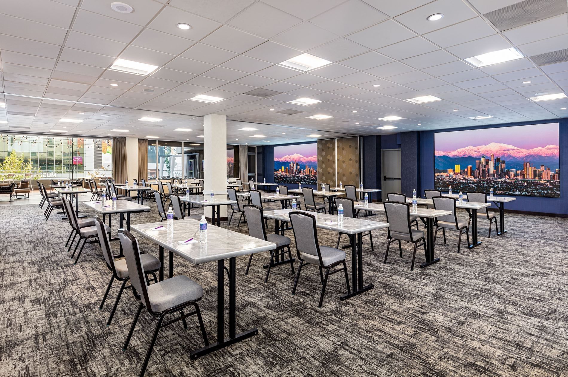 A large meeting room with rows of tables and chairs, a city view, and a white ceiling with recessed lights.