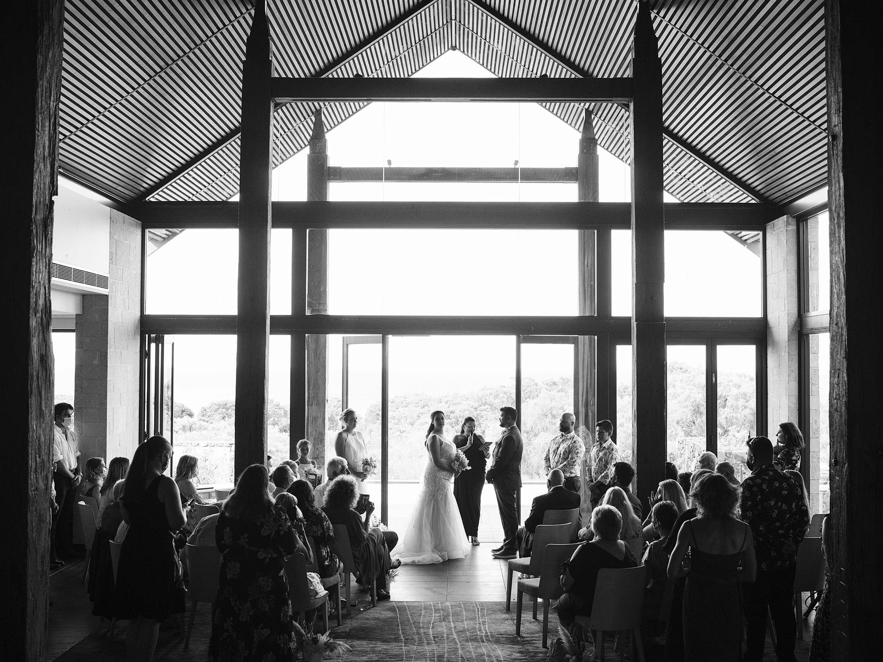 Couple exchanging vows in a sunlit, wooden-framed venue with guests seated, illustrating a winter wedding.
