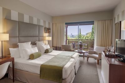 Hotel room with two beds, balcony, and furniture including chairs, table, and TV.