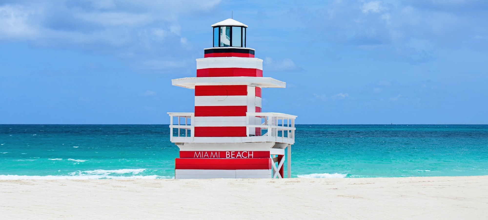 A red and white striped lighthouse on a beach with the words 'MIAMI BEACH' on it.