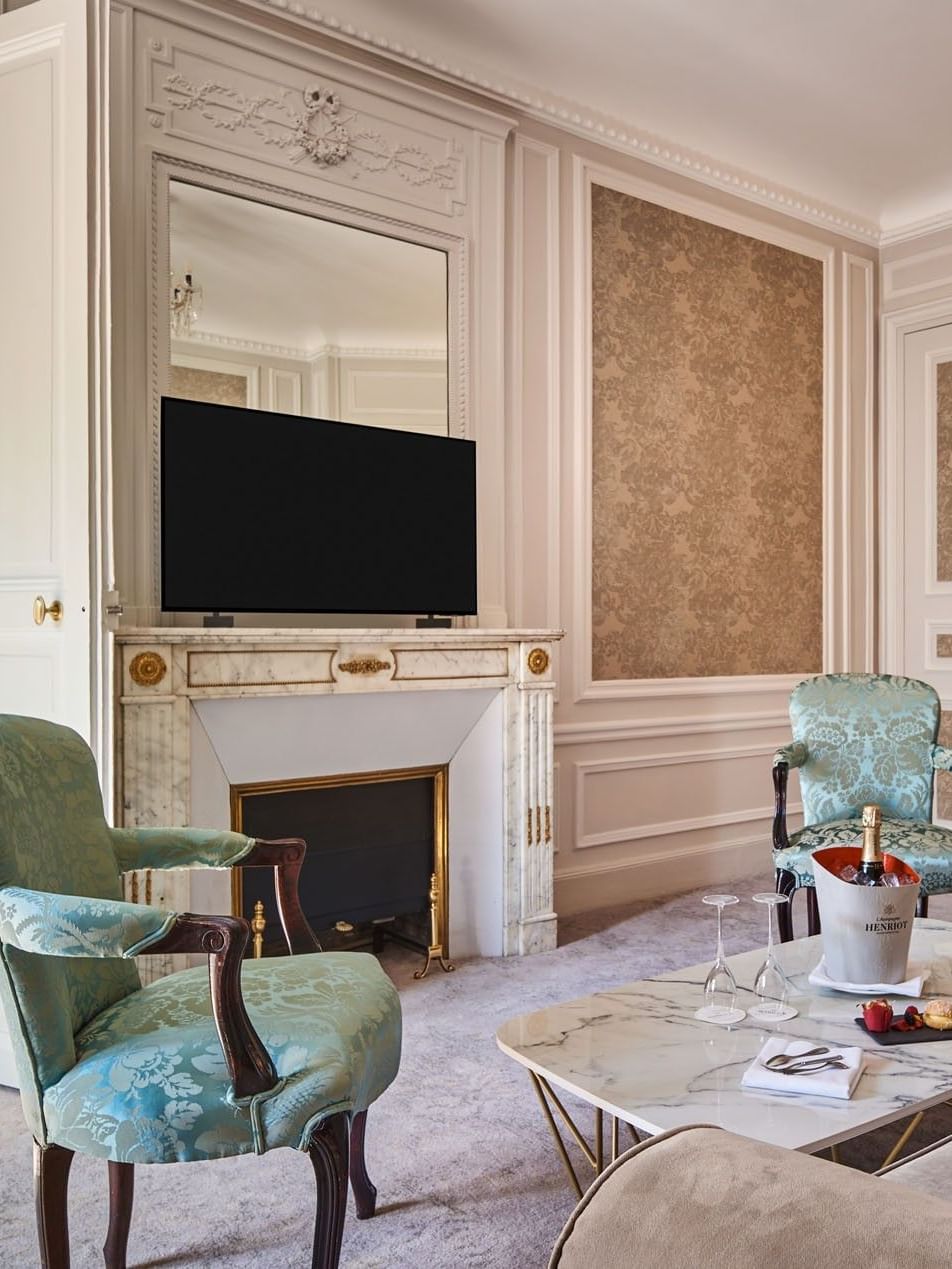 TV lounge with plush sofa and doorway to bedroom in Prestige Suite – Rue de la Paix View at Hotel Westminster Paris