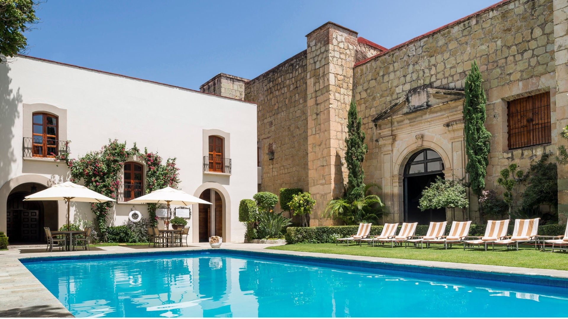 Lounge chairs by a pool under a sunlit sky surrounding stone walls in Camino Real Pedregal Mexico