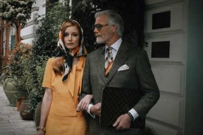 Elegant couple in a yellow dress and patterned suit stands in a lush urban setting at Hotel Motto Vienna