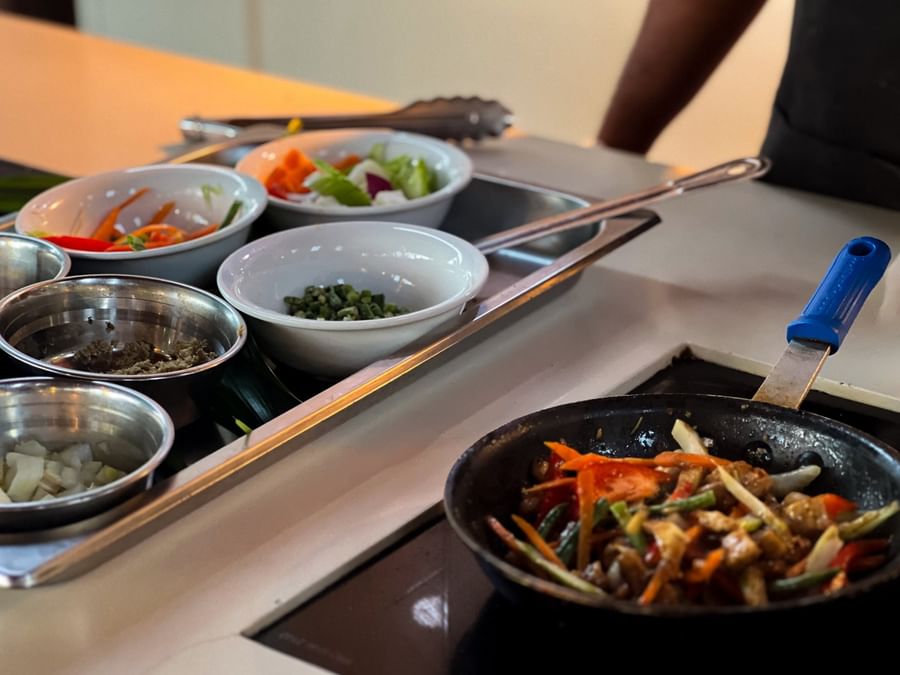 Fresh vegetables in white bowls by a sizzling pan on an induction cooktop at TokaToka Resort Nadi Fiji