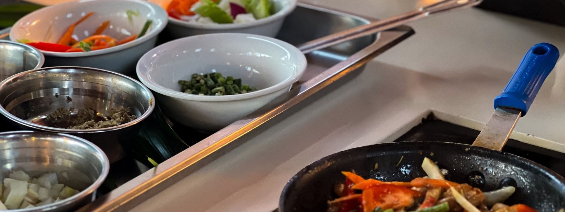 Bowls of assorted vegetables on a tray and a pan with stir-fried veggies at KanaVata Restaurant in Nadi