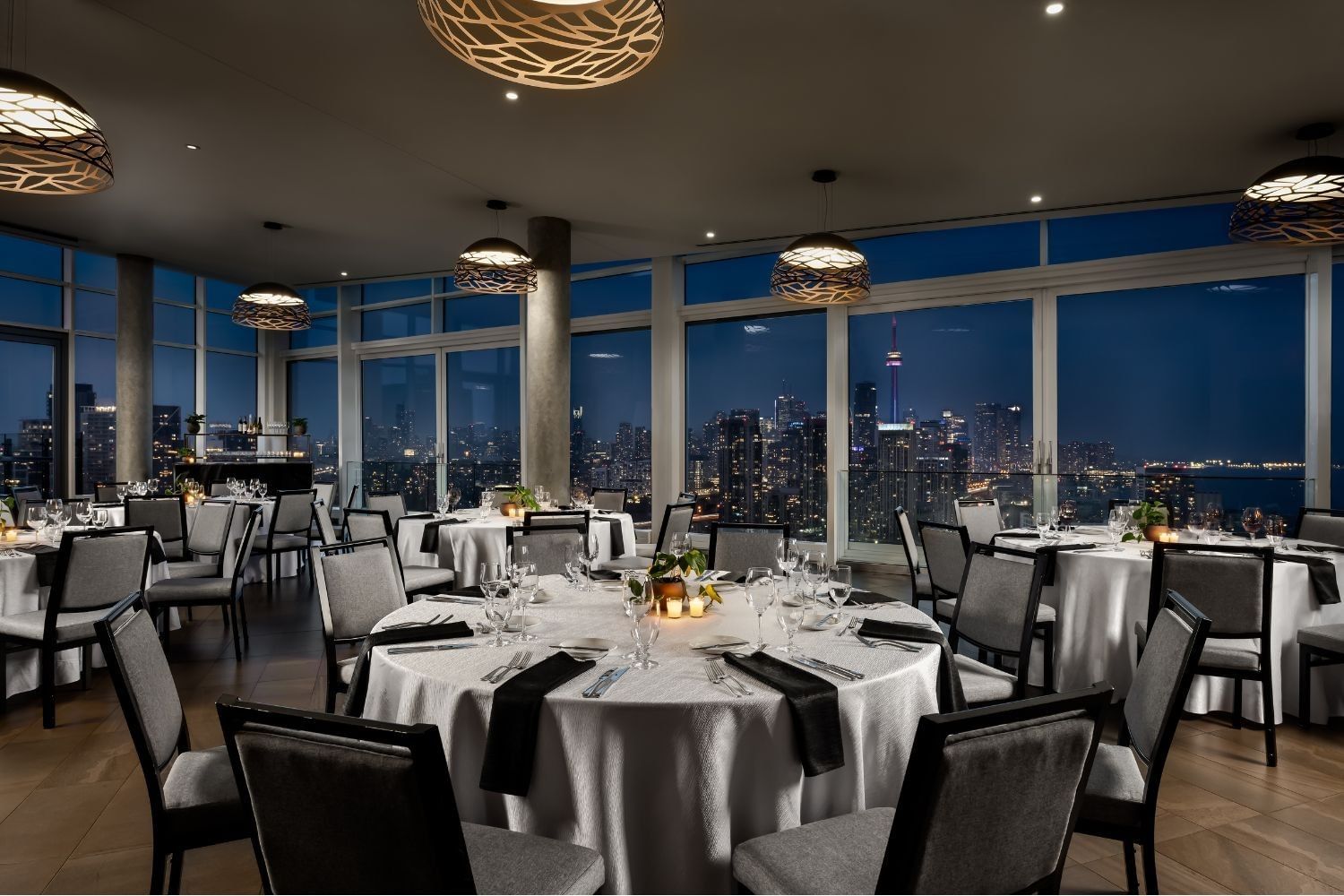 The View with round tables and grey chairs overlooking the illuminated Toronto skyline at night at Hotel X Toronto