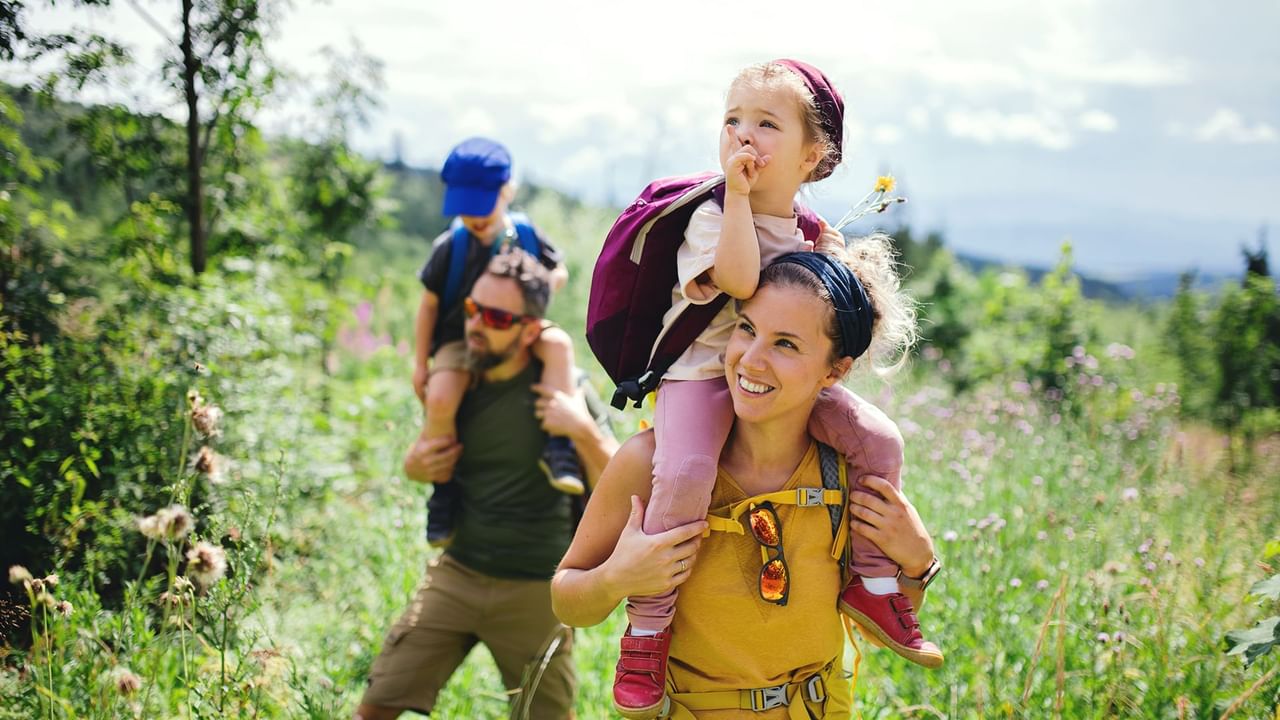 Family hiking in nature with children on shoulders.