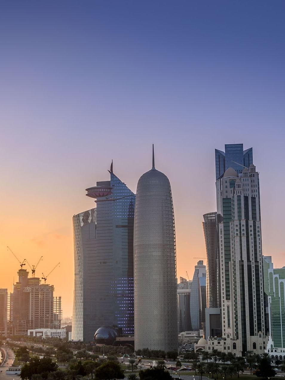 View of Doha City by a calm bay under a vibrant orange and purple sunset sky near