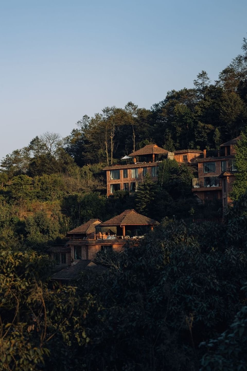 The Dwarika's Himalayan Wellbeing, nestled on a hillside, surrounded by lush trees beneath a clear blue sky