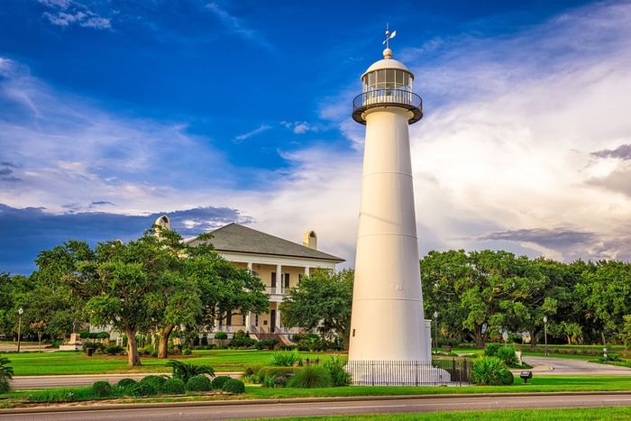 Biloxi Lighthouse standing tall against blue sky with a resort building nestled among the trees near Centennial Plaza Resort