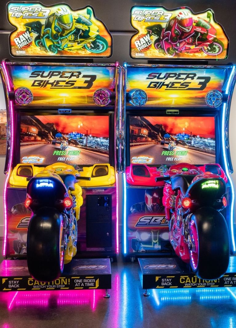 Yellow and pink Super Bikes 3 motorcycle simulators standing side by side, under neon signage at Hotel X Toronto