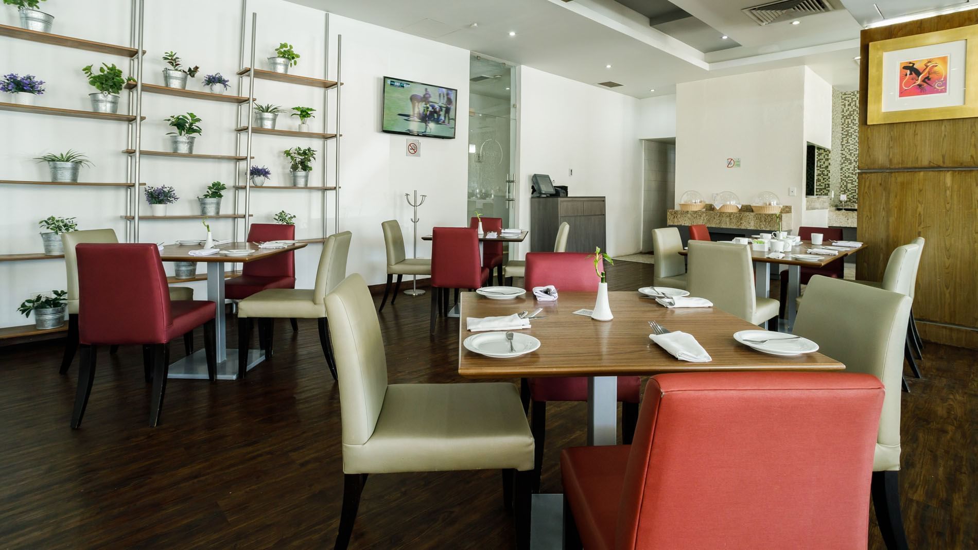 Stock Café featuring wooden tables, red chairs, and decorative plants on wall shelving at Real Inn Torreon