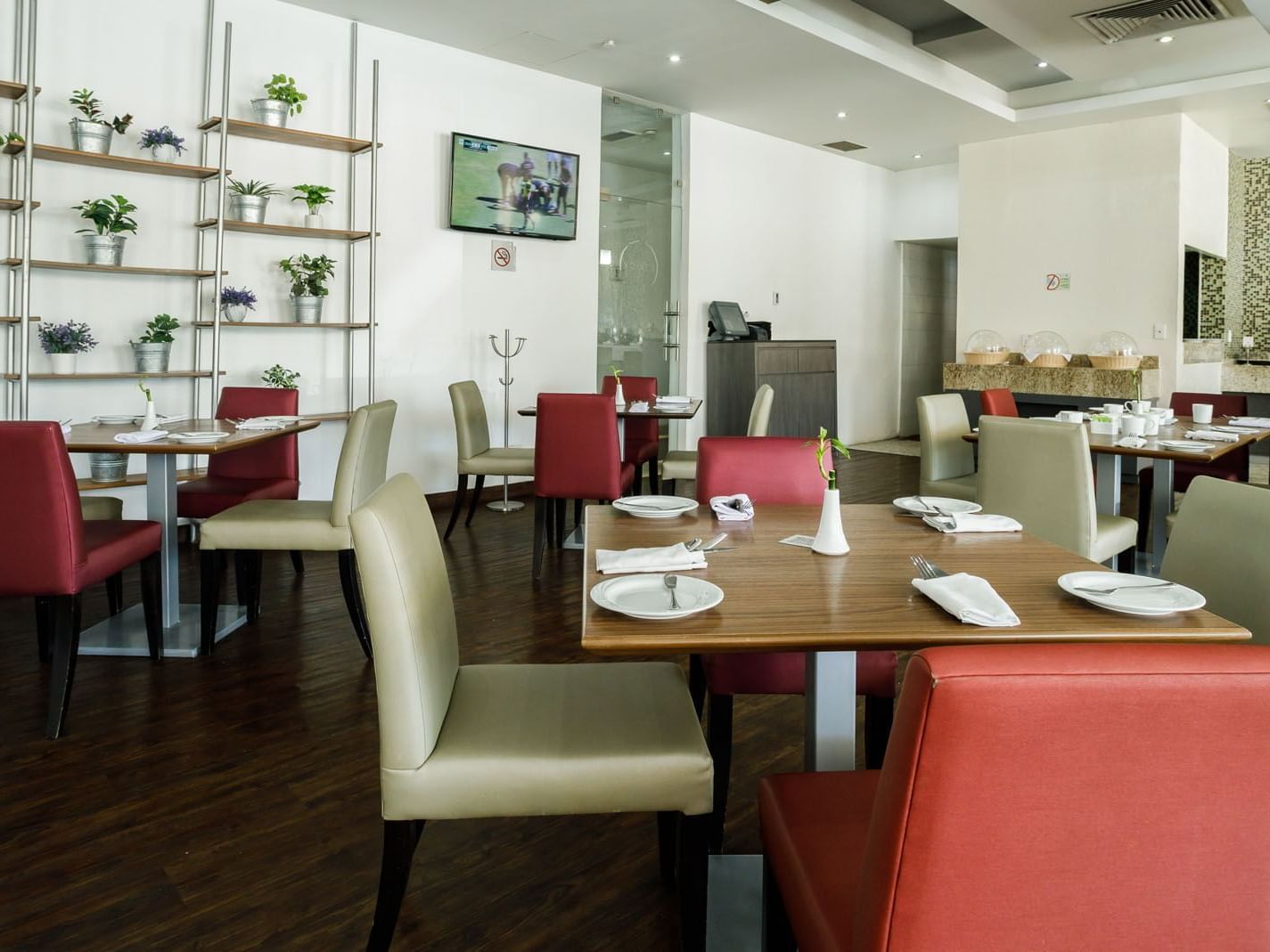Stock Café featuring wooden tables, red chairs, and decorative plants on wall shelving at Real Inn Torreon