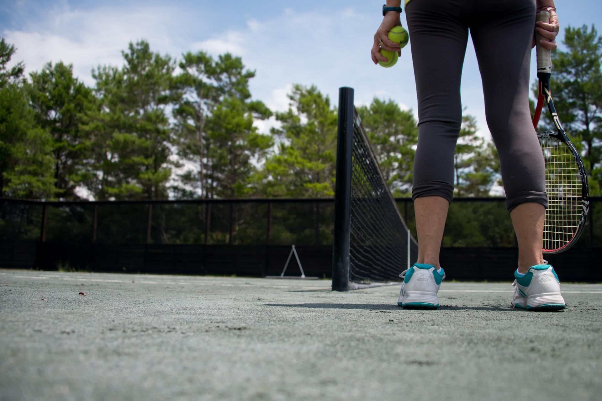 Low-angle view of a lady holding tennis balls and a racket on the court at Watersound Inn