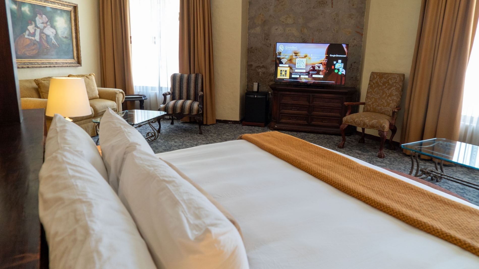 King Governor Suite Modern TV on a dresser near a stone wall, and a striped armchair at Quinta Real Aguascalientes