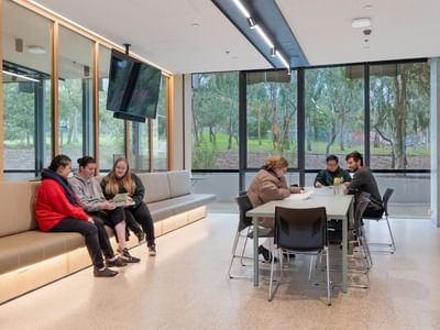 People sit on a bench and at a table in a modern La Trobe University student lounge.