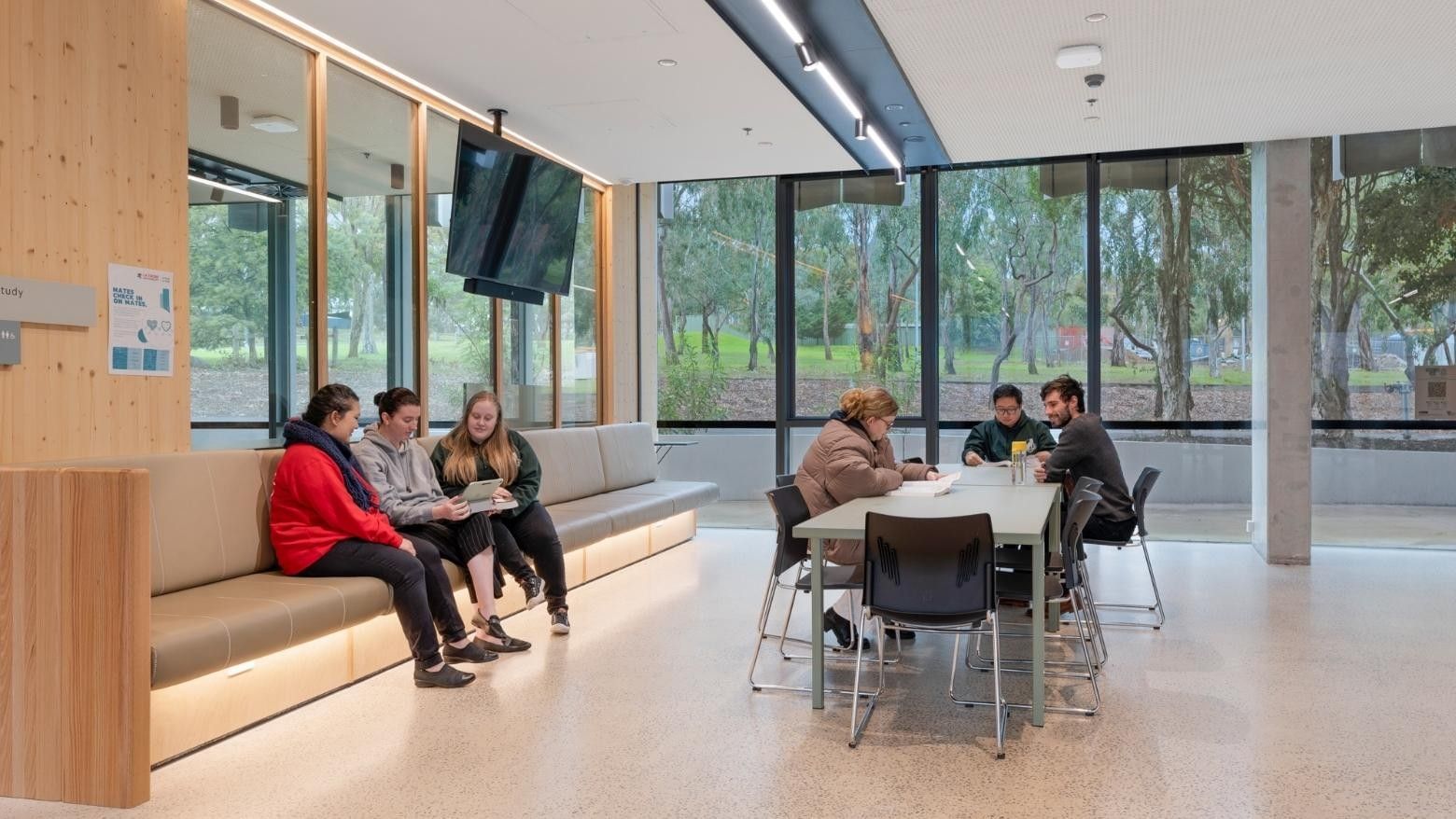 People sit on a bench and at a table in a modern La Trobe University student lounge.