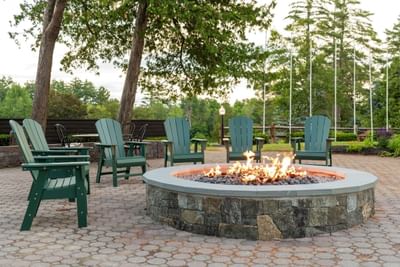 Outdoor fire pit with flames surrounded by Adirondack chairs in The Lodge at Schroon Lake