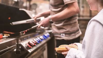 Person in striped shirt grills sausages as another readies a bun, enjoying a cookout at Blackstone Mountain Lodge
