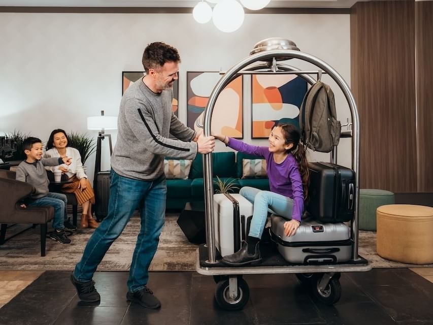 Father pushing a luggage cart with the kid sitting on it in the lobby at Sandman Hotel & Suites Winnipeg Airport