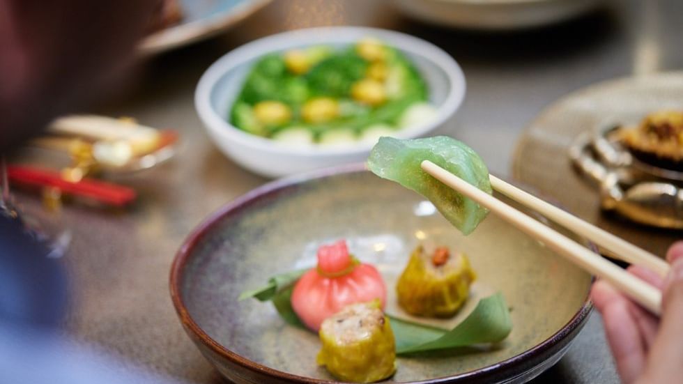 Person holding dumpling with chopsticks served in restaurant at Crown Hotels Perth