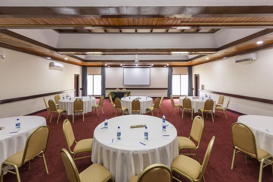 Pacific Ballroom meeting room with round tables & gold chairs, and a projector screen at warwick le lagon-vanuatu