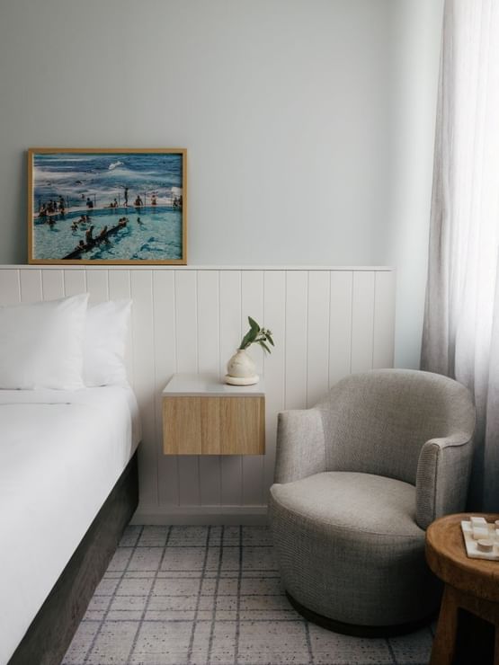 Village Queen at Elysium Manly, featuring a grey armchair by a floating nightstand under an ocean pool photo print