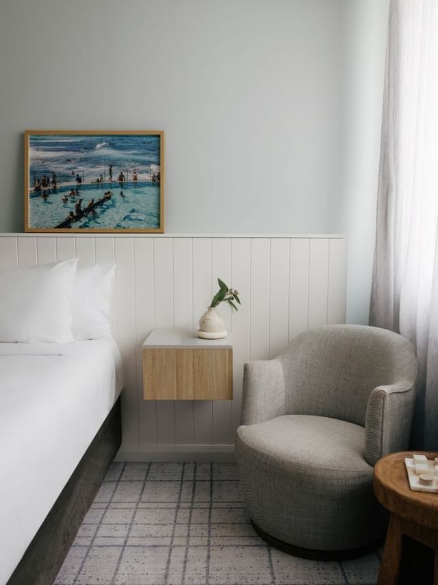 Village Queen at Elysium Manly, featuring a grey armchair by a floating nightstand under an ocean pool photo print