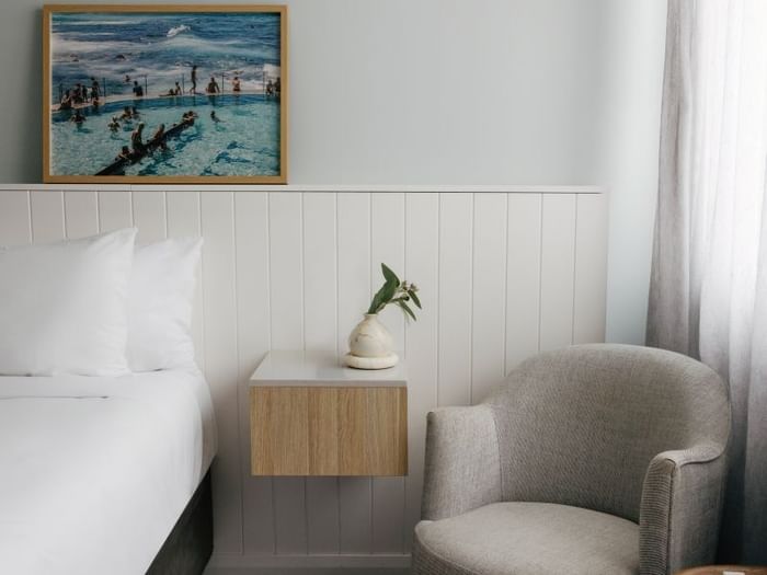 Village Queen at Elysium Manly, featuring a grey armchair by a floating nightstand under an ocean pool photo print
