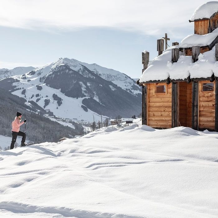 Person snowshoeing on winter slopes beside a snow covered wooden cabin in mountains at Falkensteiner Hotels & Residences