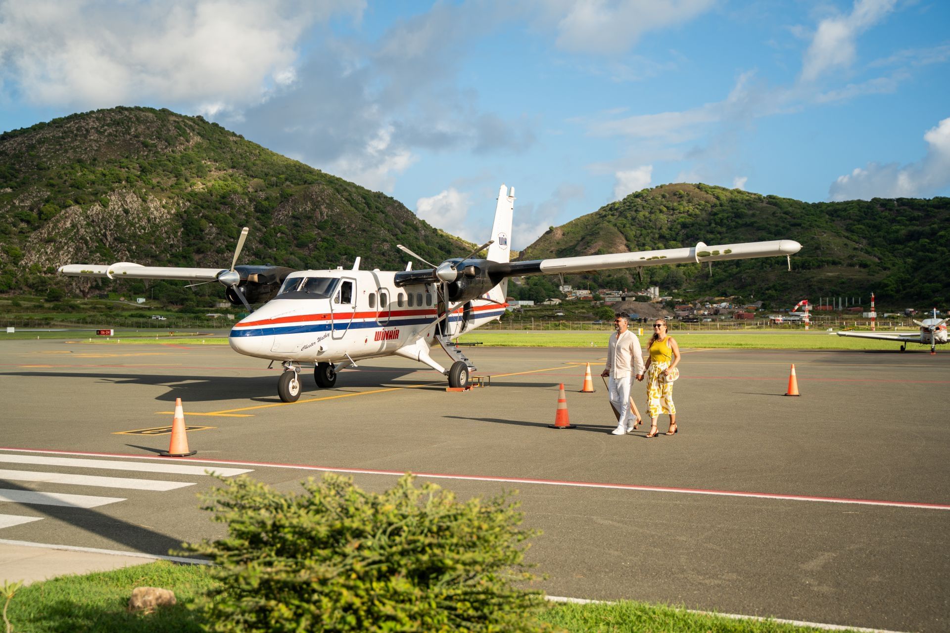 Couple walking on an airport tarmac beside a small aircraft, surrounded by lush green hills near Golden Rock Resort