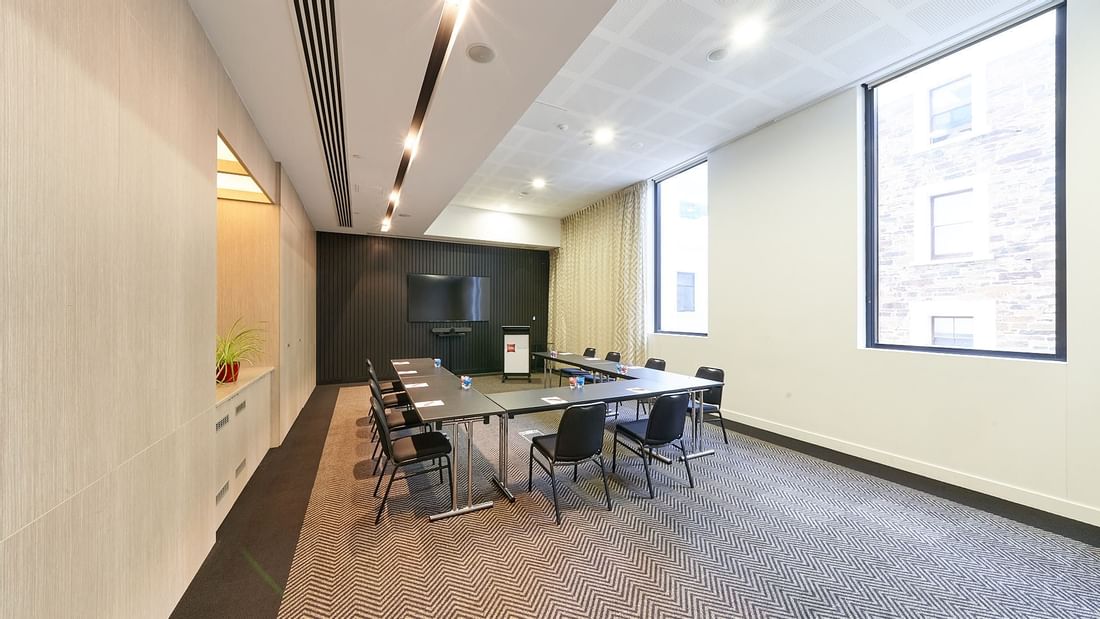 U-shape table set up facing a wall-mounted TV in The Engine Room at Ibis Adelaide