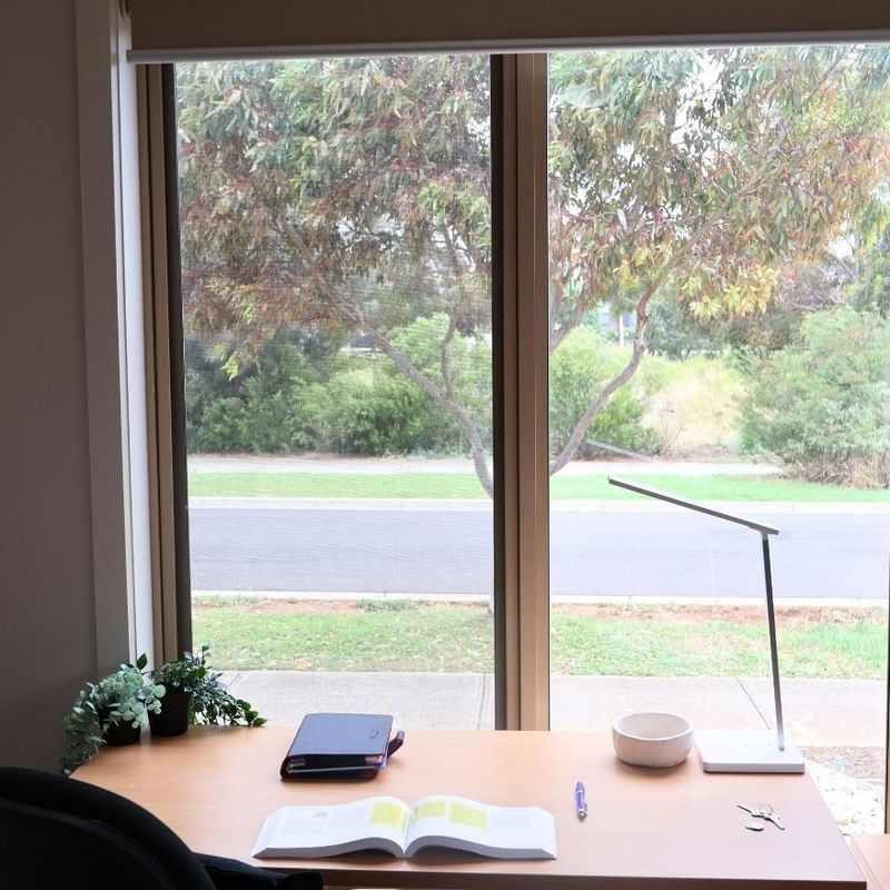 A cozy study area with a desk, open book, and scenic window view at La Trobe University Regional Housing – Melton.