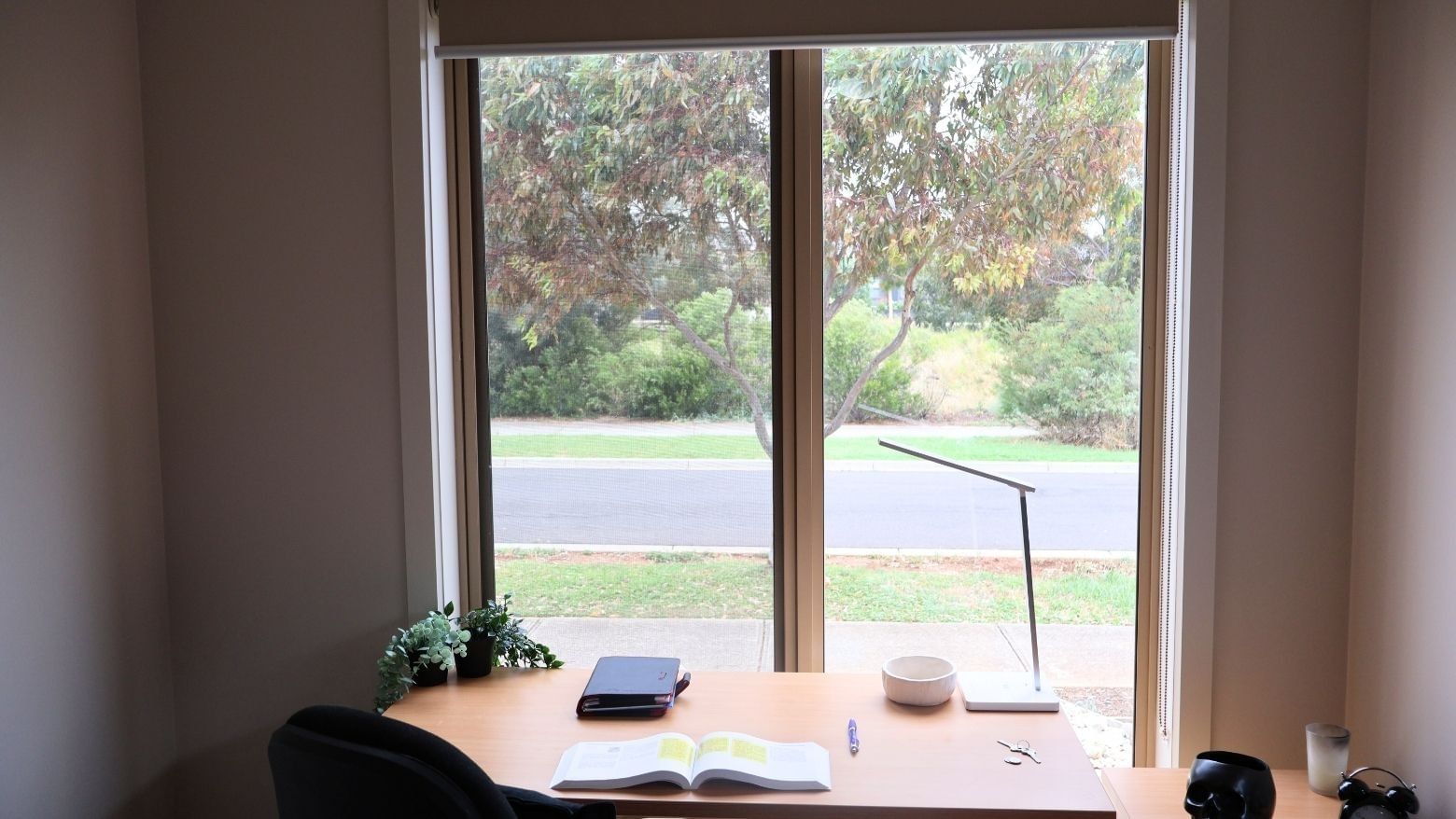 A cozy study area with a desk, open book, and scenic window view at La Trobe University Regional Housing – Melton.