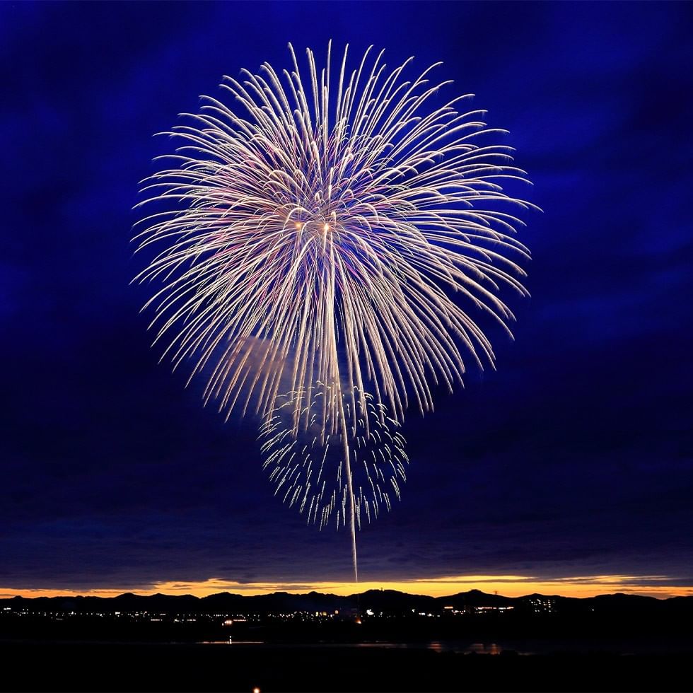 Fuochi d'artificio a forma di cuore esplodono nel cielo notturno sopra una città illuminata.