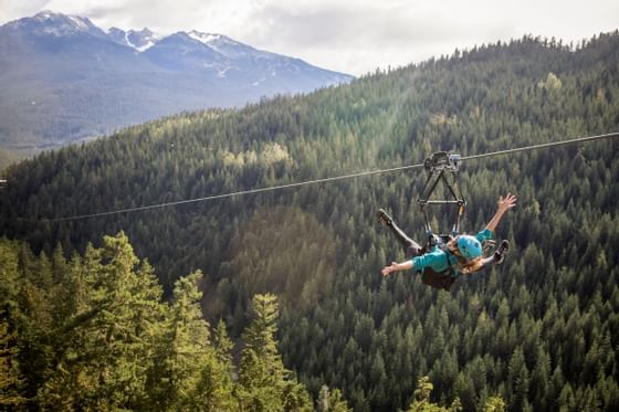 Person soaring on a zipline through the lush greenery mountains near Blackcomb Springs Suites