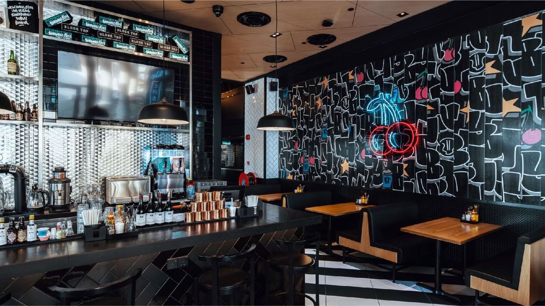 Trendy bar interior at Sunway Hotel Pyramid with neon art, booths, and a counter, promoting happy hour offer